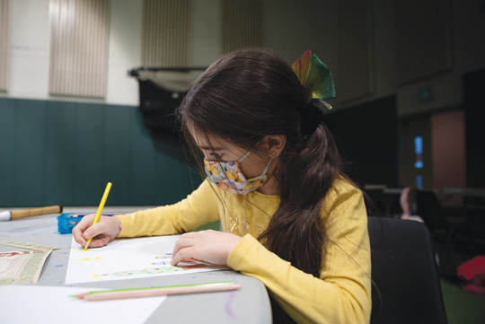 A young girl with long dark hair colours on a piece of paper.