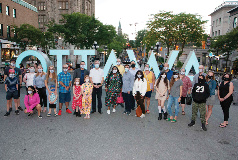 A group of people — both adults and children — stand in front of the Ottawa sign downtown.