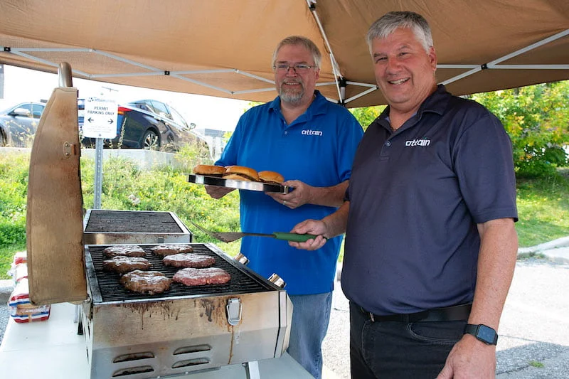 Two men enjoy barbecuing some hamburgers at a work function
