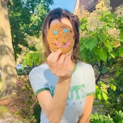 A woman holds a cookie decorated with a smile in front of her face