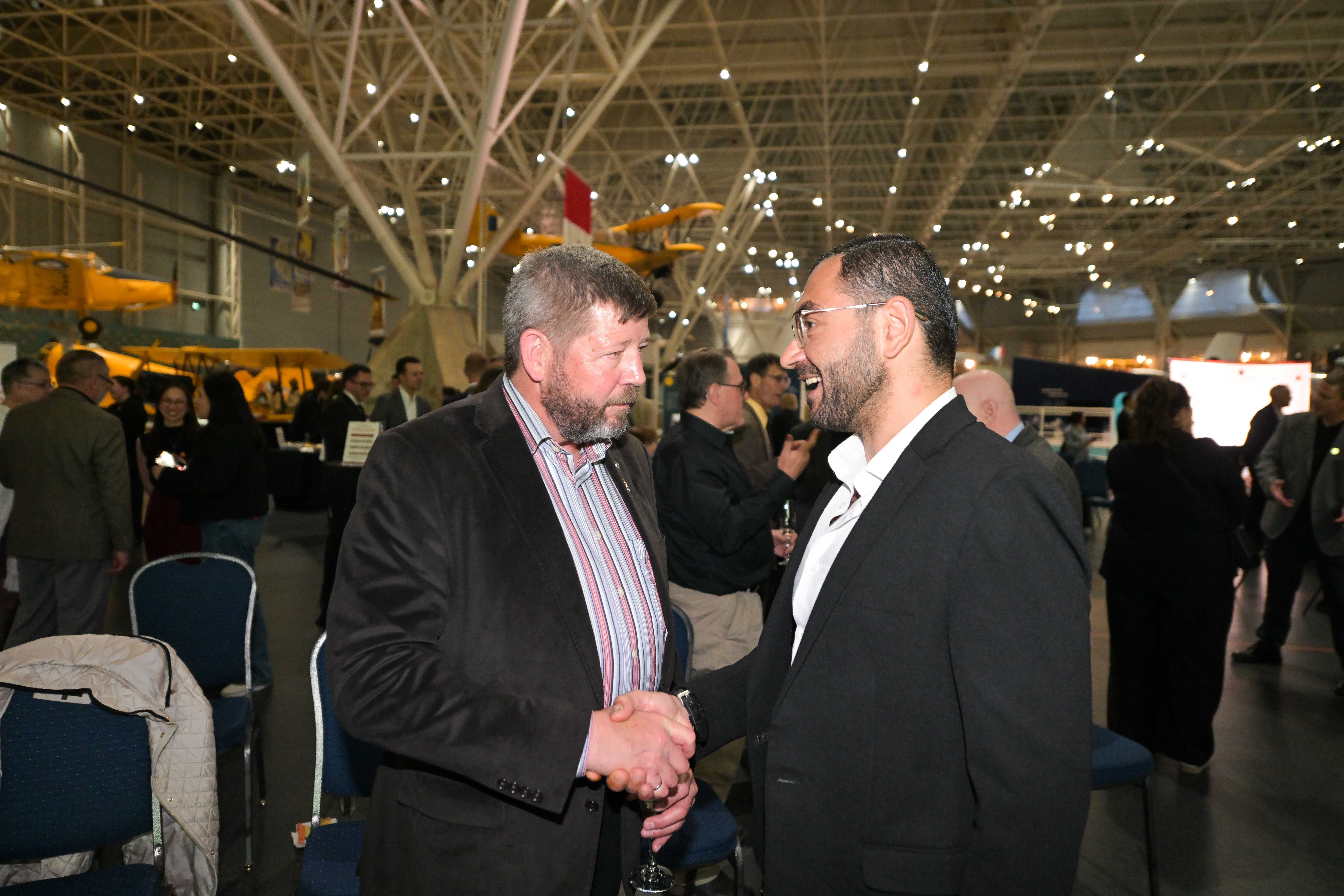 Alan Mulawyshyn (Executive Director, VHC) and Ala’a Shadid (Executive Director, Multifaith Housing Initiative) greet one another during Veterans’ House Canada’s Andy Carswell Building 5th Anniversary celebration at the Canadian Aviation and Space Museum. Photo by James Park.